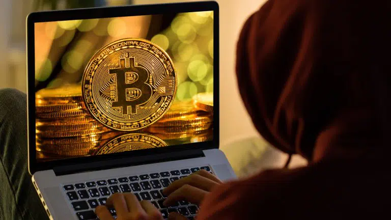 Moeda de Bitcoin e hacker anônimo sentado com laptop
