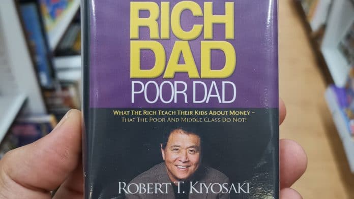 Uma mão segurando um famoso livro de Pai Rico, Pai Pobre na livraria