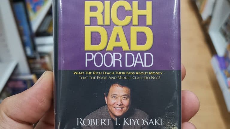 Uma mão segurando um famoso livro de Pai Rico, Pai Pobre na livraria
