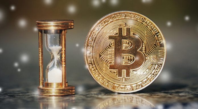 Ampulheta e moeda física de Bitcoin.