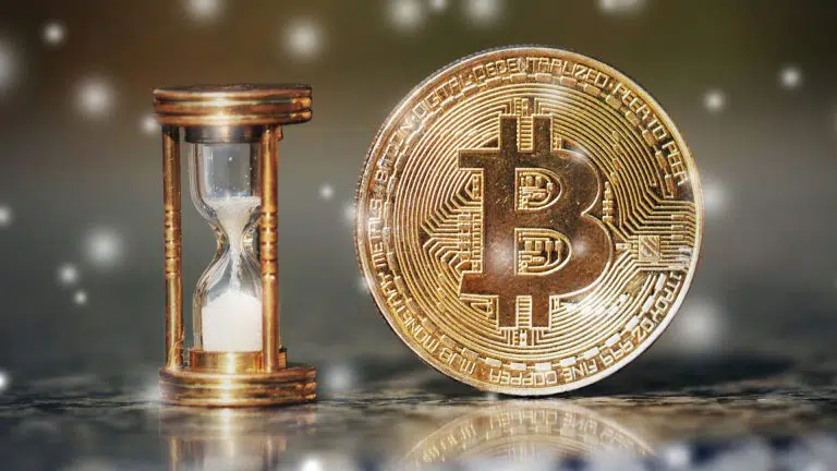 Ampulheta e moeda física de Bitcoin.