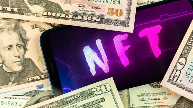 Celular com palavra NFT próximo de notas de dinheiro