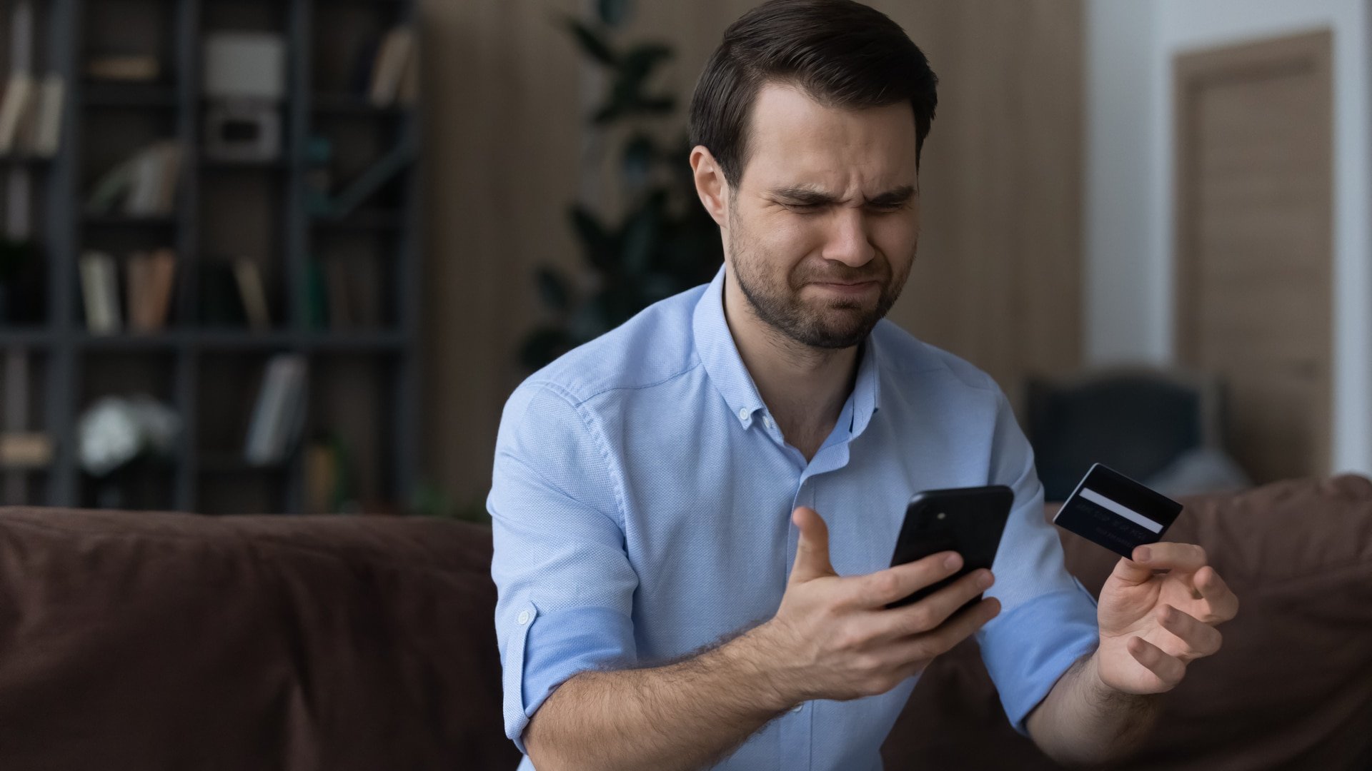 Homem frustrado por problemas com banco, segurando celular e cartão