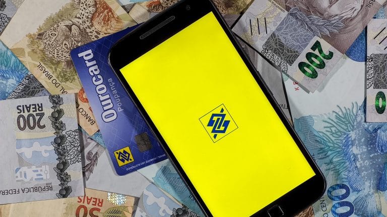 Imagem do aplicativo do Banco do Brasil, com cartão de crédito e dinheiro ao fundo