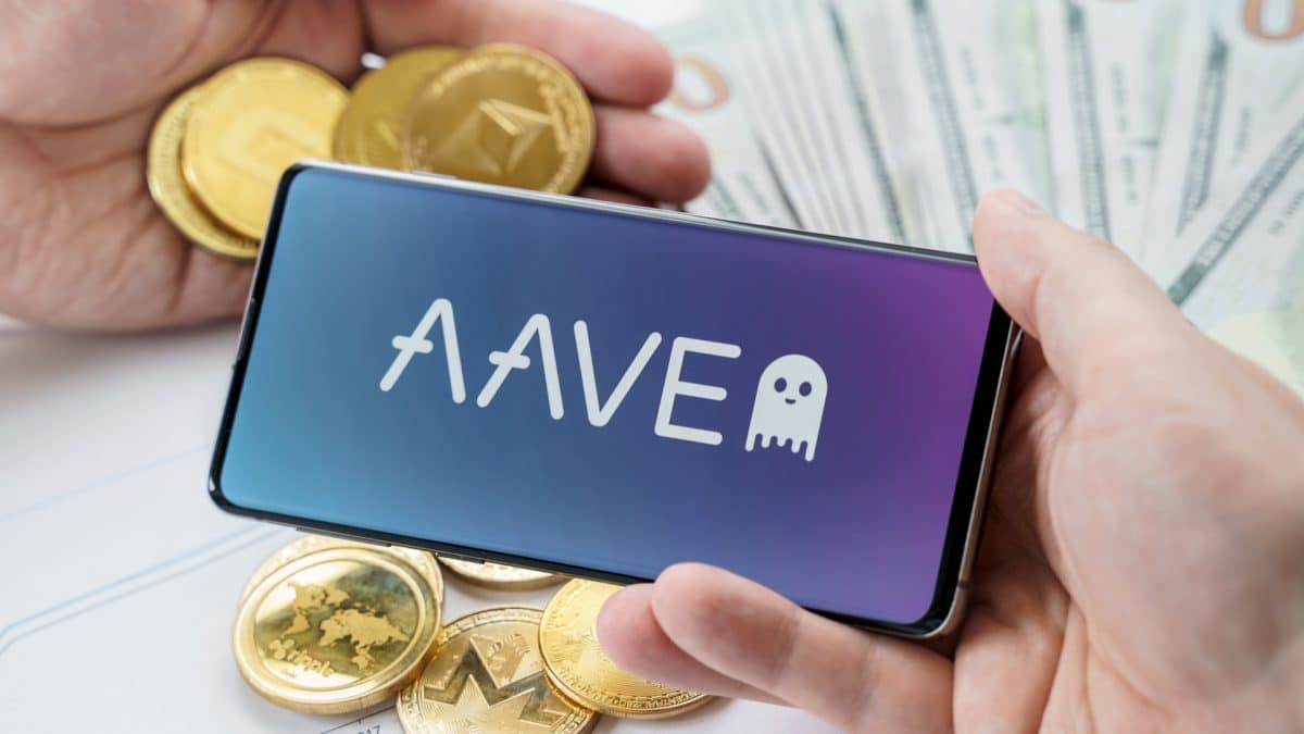 Logo AAVE no celular com criptomoedas em volta