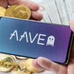 Logo AAVE no celular com criptomoedas em volta