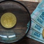 Lupa de olho em Bitcoin próxima de notas de Real do Brasil