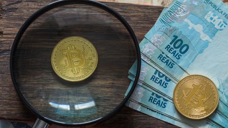 Lupa de olho em Bitcoin próxima de notas de Real do Brasil