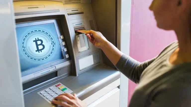 Mão de mulher inserindo cartão bancário no caixa eletrônico com bitcoin