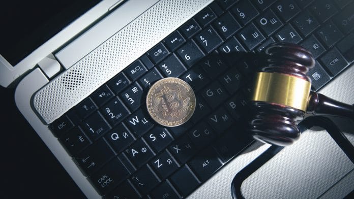 Martelo da justiça em cima de notebook e ao lado de Bitcoin