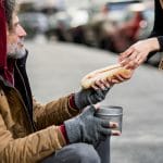 Mulher irreconhecível dando comida para mendigo sem-teto sentado na cidade