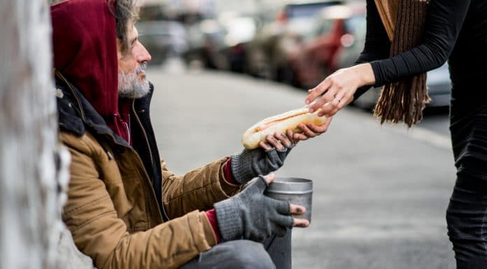 Mulher irreconhecível dando comida para mendigo sem-teto sentado na cidade