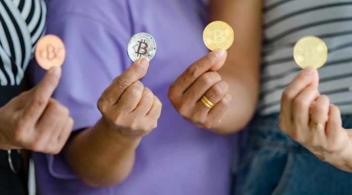 Quatro pessoas segurando moedas físicas de Bitcoin.
