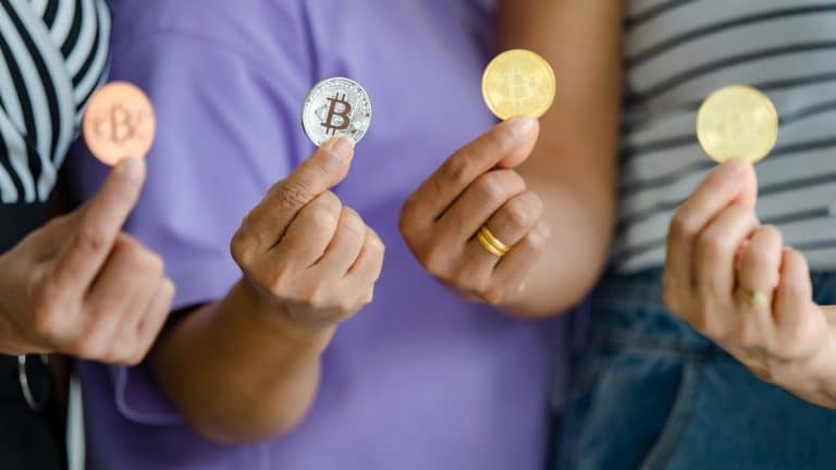 Quatro pessoas segurando moedas físicas de Bitcoin.