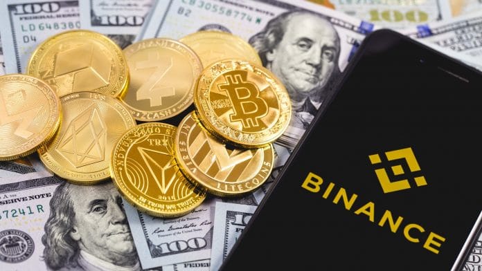 Aplicativo da Binance ao lado de criptomoedas e notas de Dólar