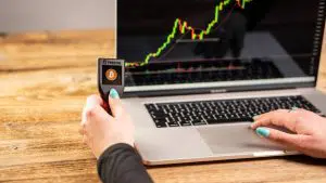 Carteira de Bitcoin Trezor ao lado de gráfico de negociações
