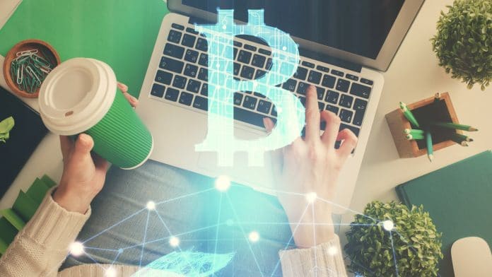 Computador com imagem de Bitcoin e mulher segurando copo de café