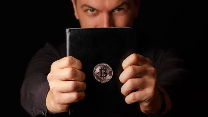 Homem segurando livro com imagem do Bitcoin colada nele pastor