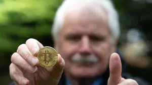 Idoso fazendo sinal de positivo com Bitcoin em mãos