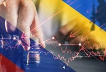 Mão segurando moedas com gráficos próximo de bandeiras da Rússia e Ucrânia