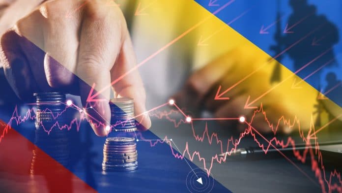 Mão segurando moedas com gráficos próximo de bandeiras da Rússia e Ucrânia