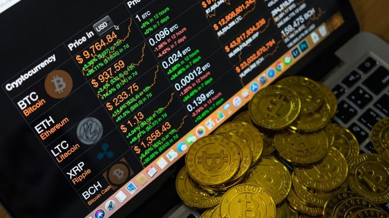 Tela de corretora de criptomoedas em computador com Bitcoins em cima do teclado