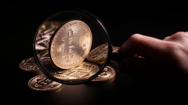 Lupa analisando moeda física de Bitcoin.