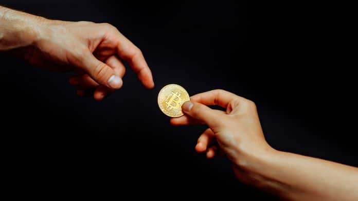 Moeda física de Bitcoin sendo passada para outra pessoa.