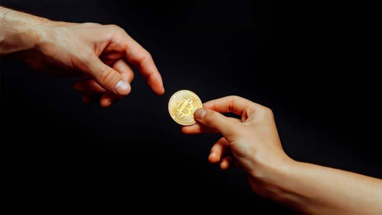 Moeda física de Bitcoin sendo passada para outra pessoa.