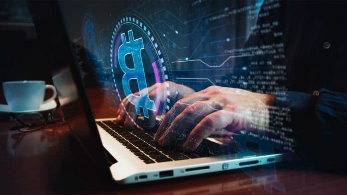 Pessoa usando notebook com logotipo do Bitcoin em forma holográfica.
