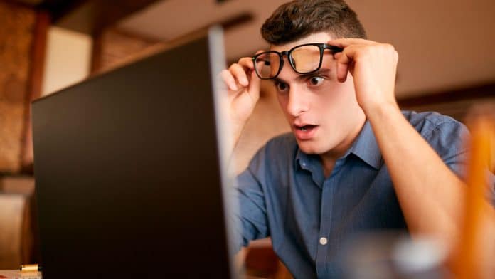 Homem espantado ao olhar para tela de computador.