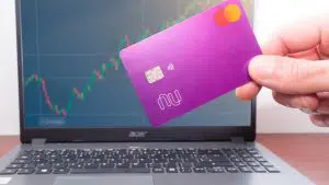 Cartão Nubank próximo de gráfico de preços em computador compra e venda bitcoin ethereum criptomoedas