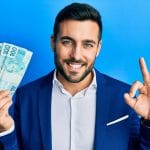 Empresário vestindo terno segurando notas reais brasileiras fazendo sinal ok