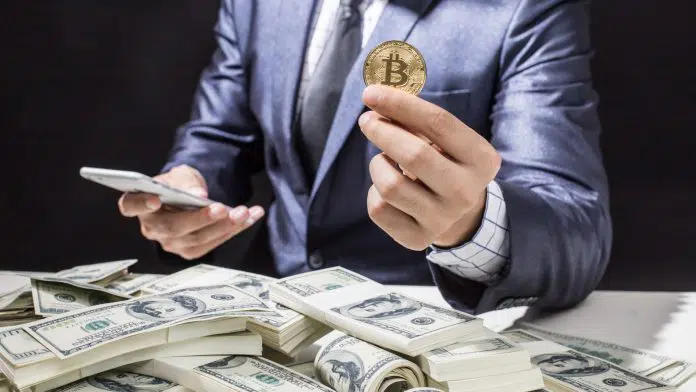 Homem segurando bitcoin próximo de notas de Dólar