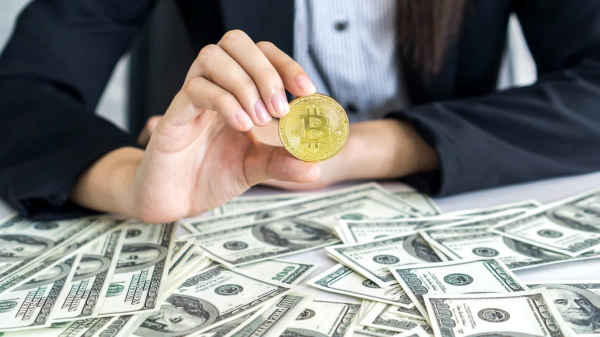 Mão segurando bitcoin em meio a dólares