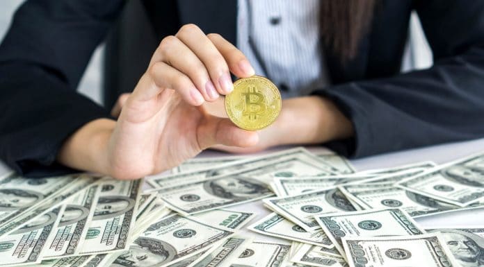 Mão segurando bitcoin em meio a dólares