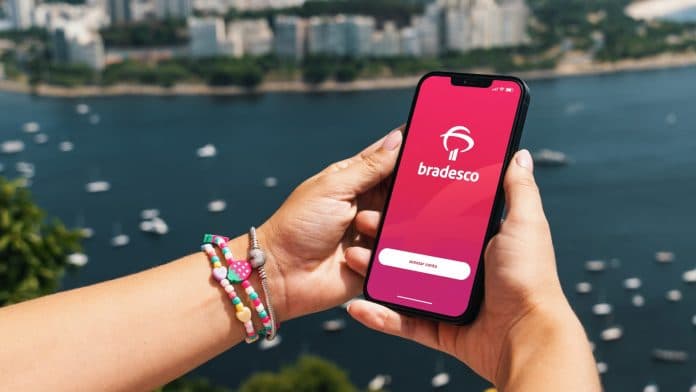 Mulher segurando smartphone com aplicativo do banco Bradesco e Rio de Janeiro ao fundo