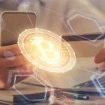 Pessoa segurando smartphone e cartão próximo de bitcoin