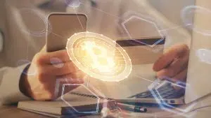 Pessoa segurando smartphone e cartão próximo de bitcoin