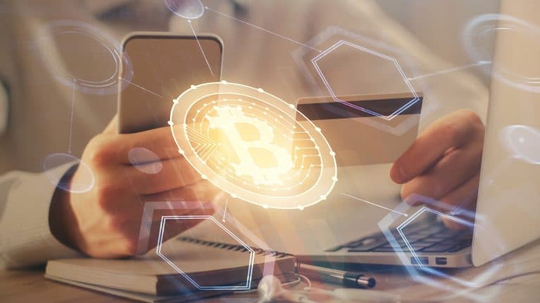 Pessoa segurando smartphone e cartão próximo de bitcoin