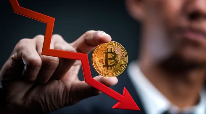 Homem segurando moeda de Bitcoin (BTC) e seta apontando queda do mercado.