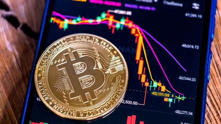 Moeda física de Bitcoin sobre gráfico de preços caindo.