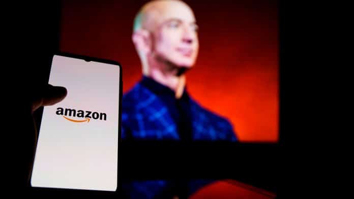 Celular com logo da Amazon na frente de foto de Jeff Bezos, fundador da empresa.