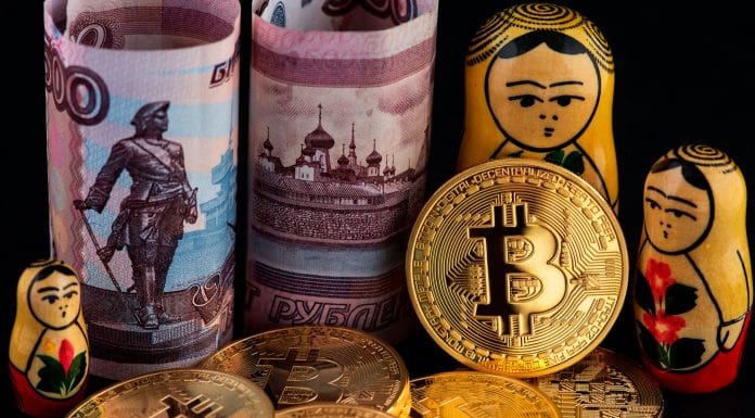 Moedas físicas de Bitcoin ao lado de rublos da Rússia e matrioskas.