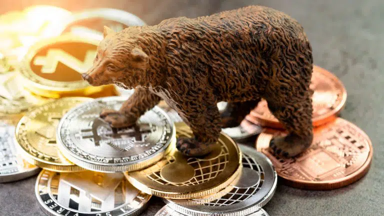 Urso em cima de moedas físicas de Bitcoin e outras criptos, representando um mercado de baixa.