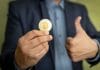 Bitcoin em uma mão com sinal de positivo na outra