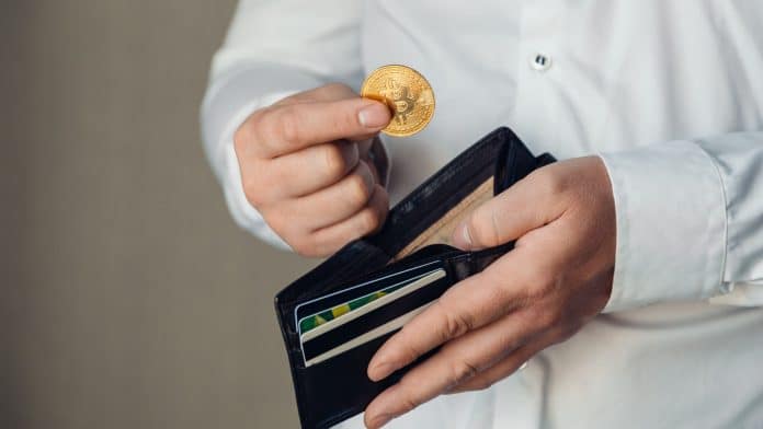 Mãos de um trabalhador colocando bitcoin em uma carteira vazia