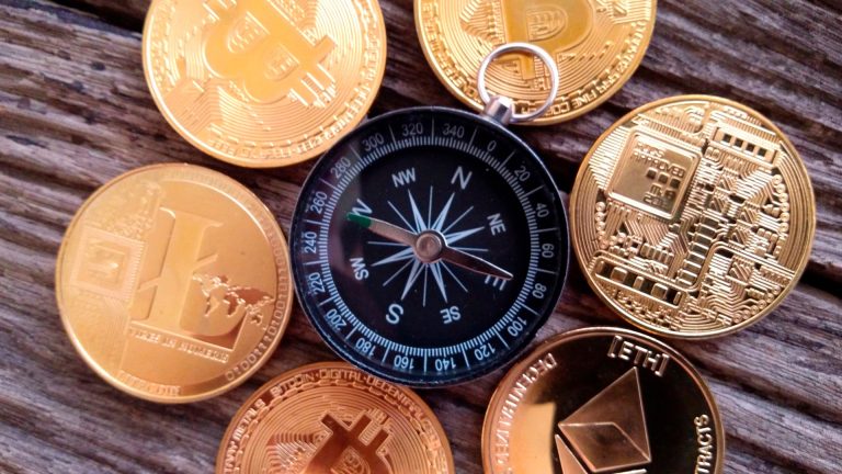 Bússola cercada por moedas físicas de Bitcoin e outras criptomoedas.