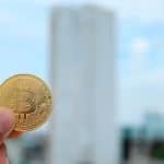 Pessoa segurando moeda de Bitcoin ao ar livre.