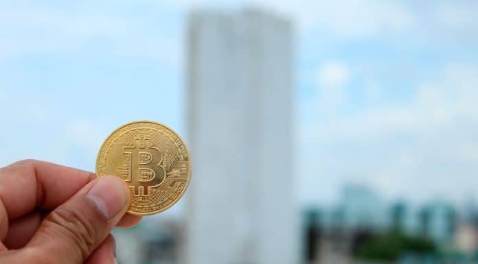 Pessoa segurando moeda de Bitcoin ao ar livre.